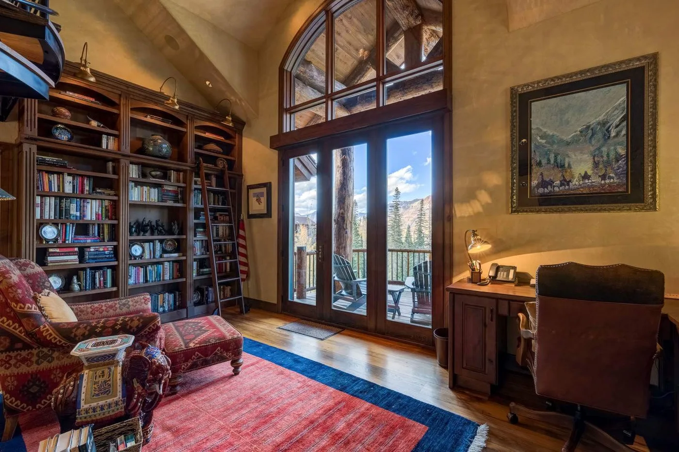 A study with bookshelves, seating, and tall glass doors opening onto a balcony.