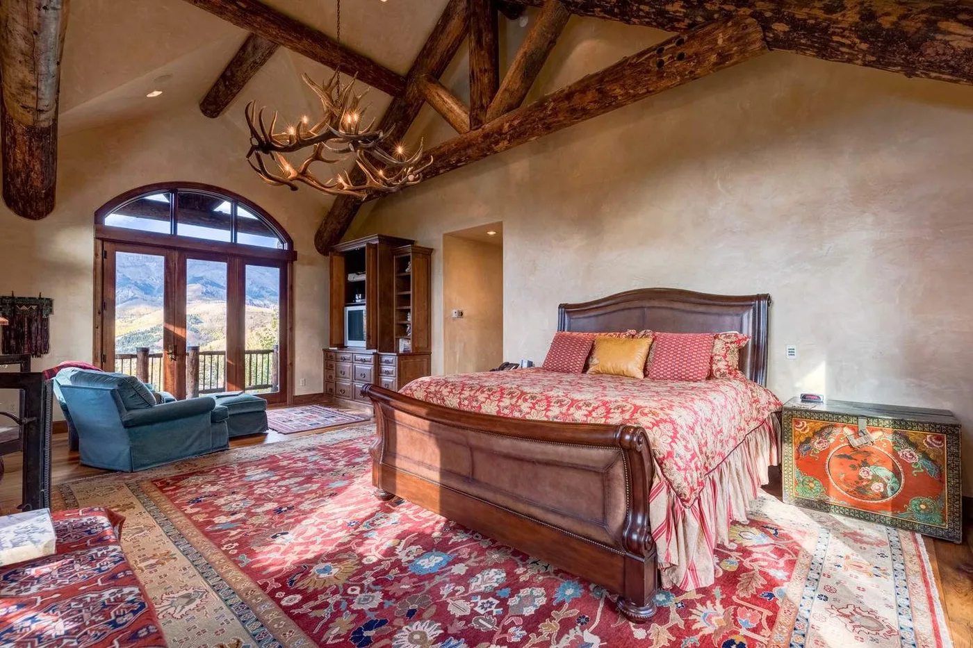 A bedroom with a large bed, patterned rugs, and exposed ceiling beams.