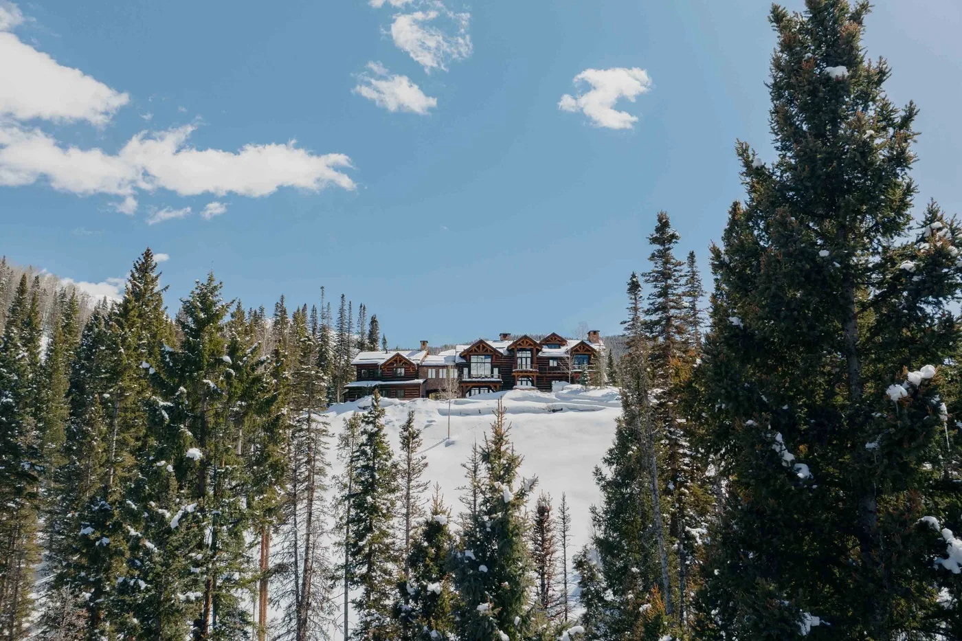 A large lodge sits on a snowy hillside among evergreen trees.