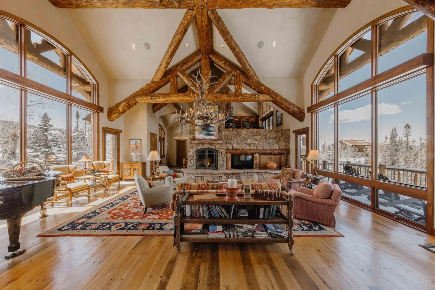 A spacious living room with exposed timber beams, large windows, and a stone fireplace.