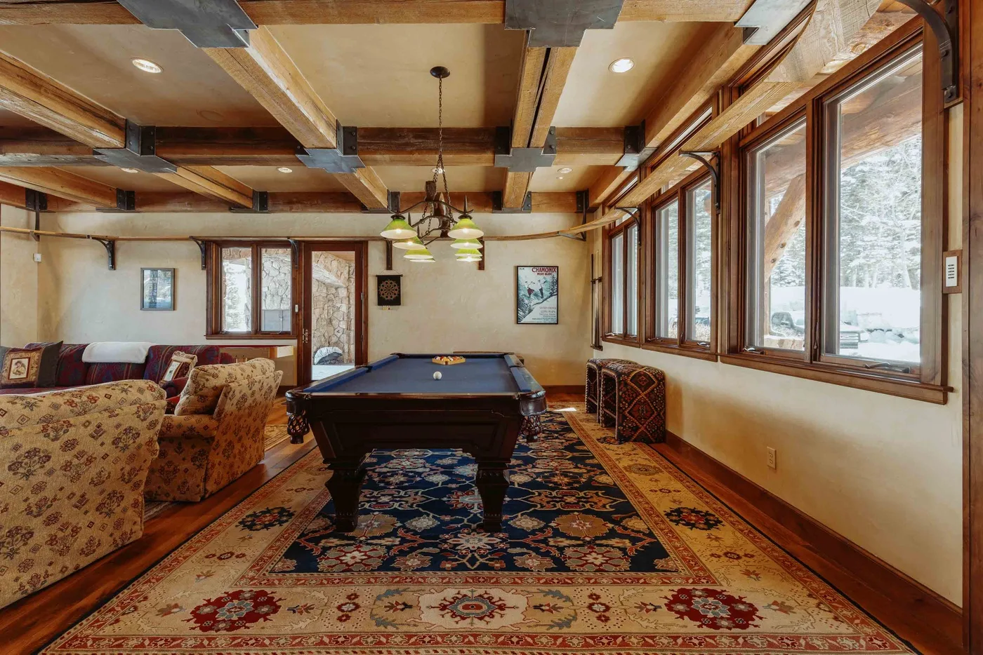 A billiards room with a pool table, patterned rug, and large windows.