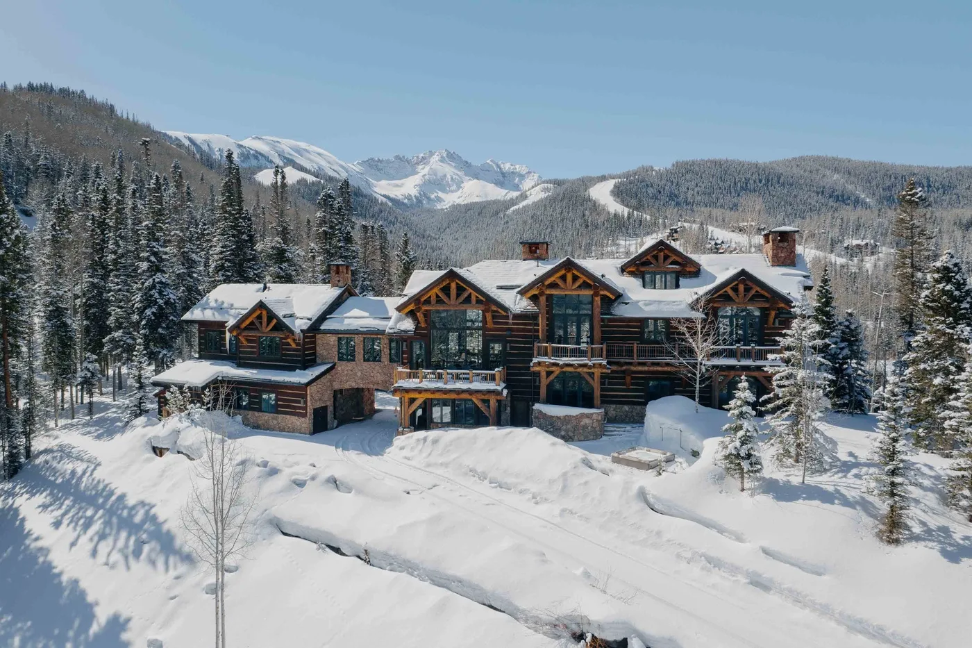 A large lodge stands amid snow-covered trees, with mountains rising in the background.