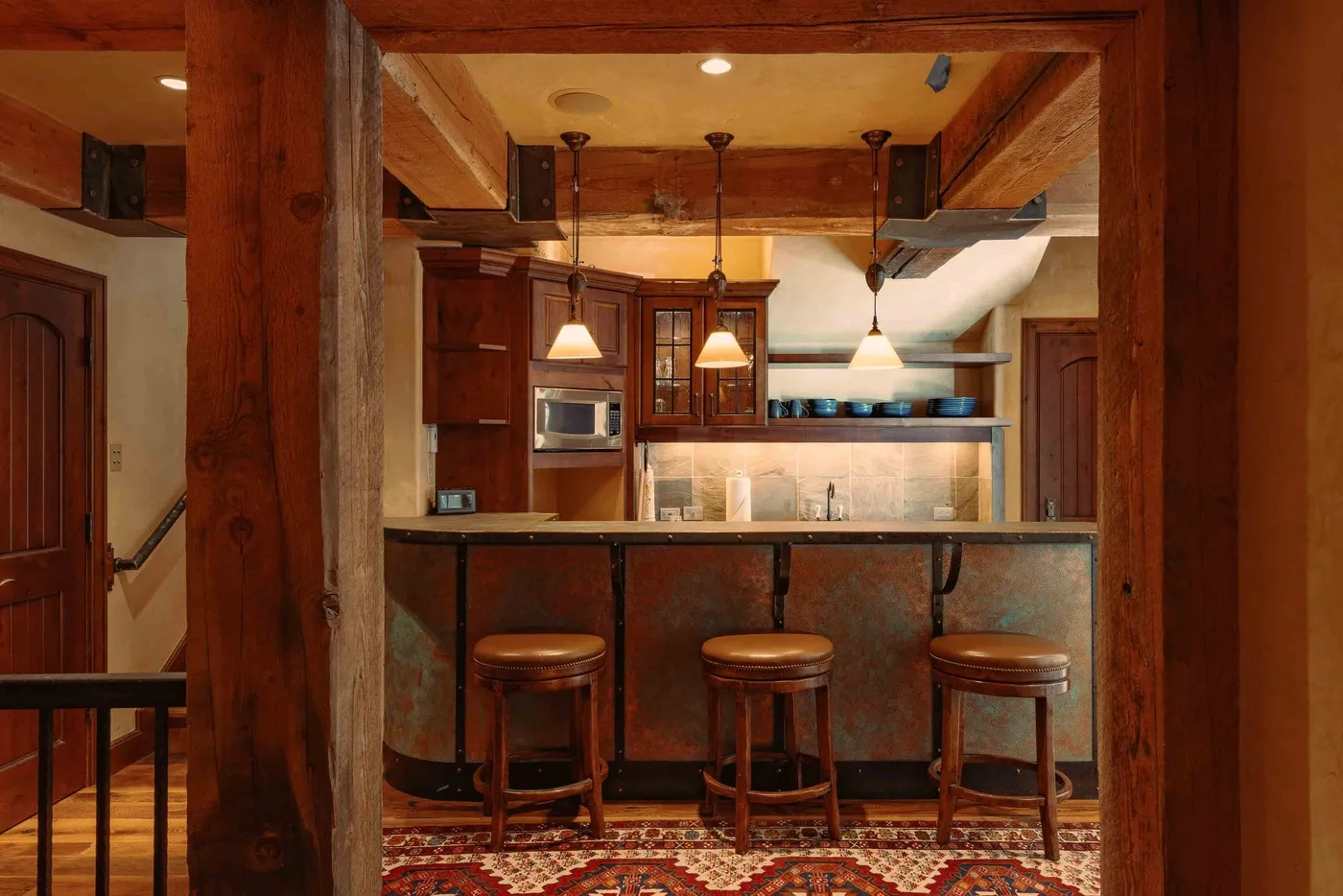 A bar area with three stools sits in front of a wood-paneled kitchen.
