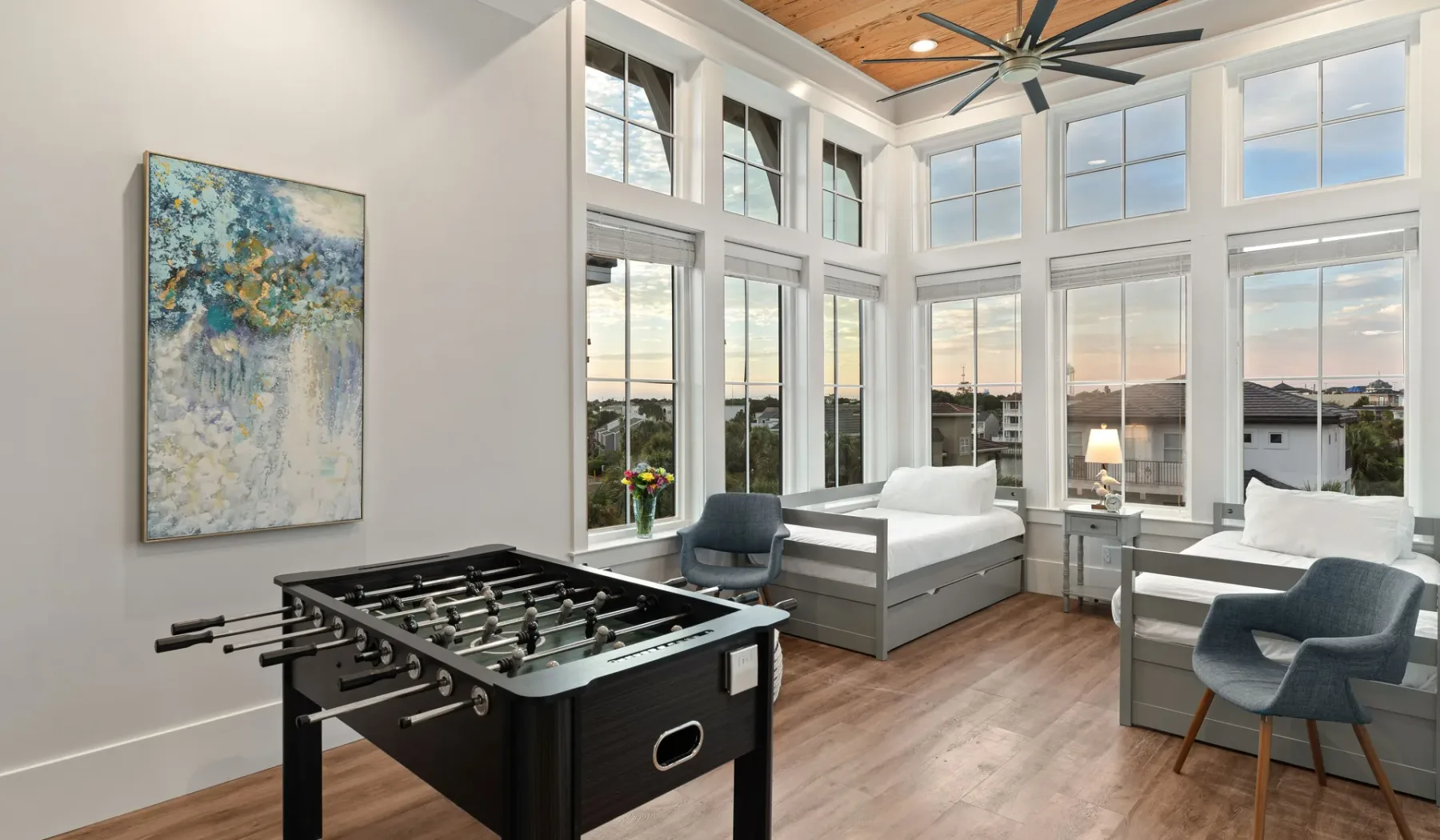 Una habitación luminosa con grandes ventanas, asientos y una mesa de futbolín.
