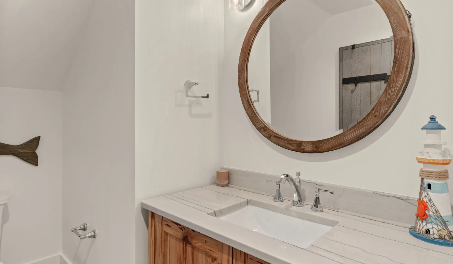 Un tocador de baño con lavabo, espejo redondo y adornos náuticos.