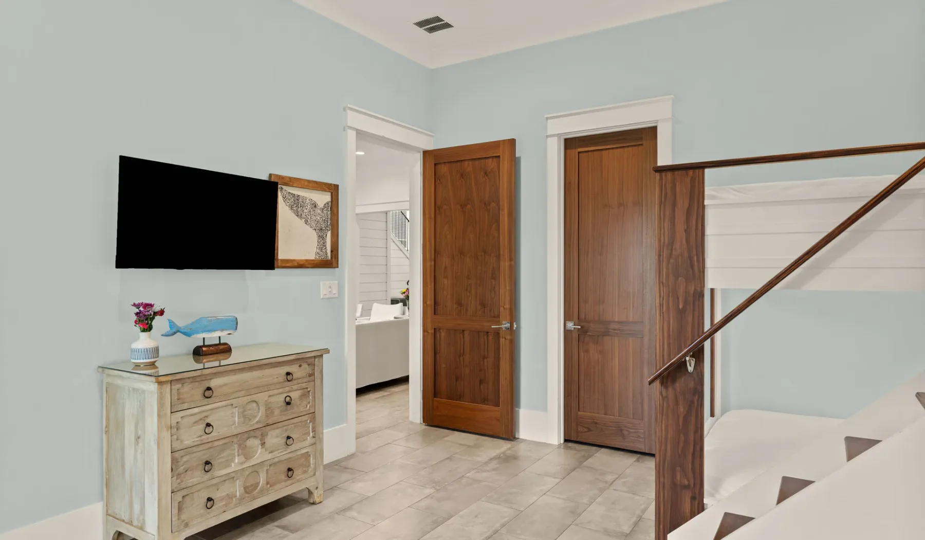 Una habitación de tonos claros con puertas de madera, una cómoda y una escalera.