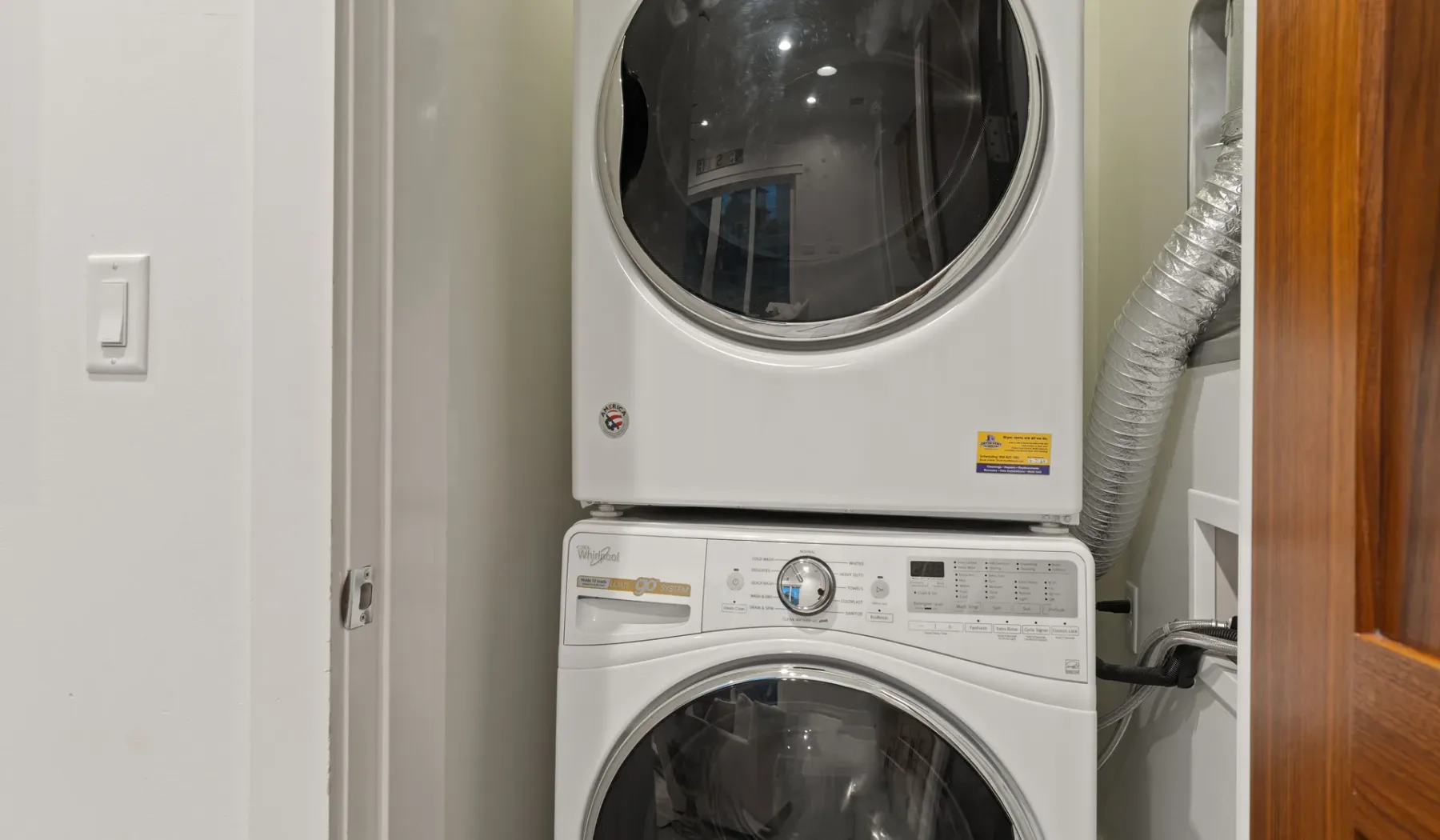 Un área de lavandería con lavadora y secadora apiladas junto a una puerta de madera.