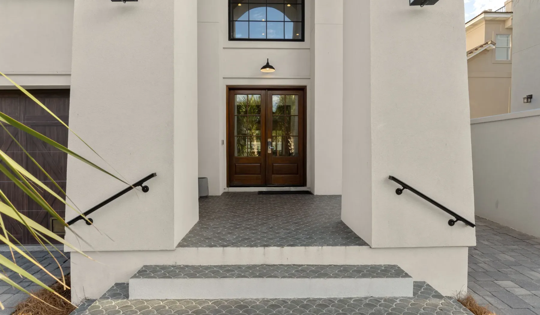 Una entrada exterior tiene puertas dobles oscuras que dan a un camino pavimentado.