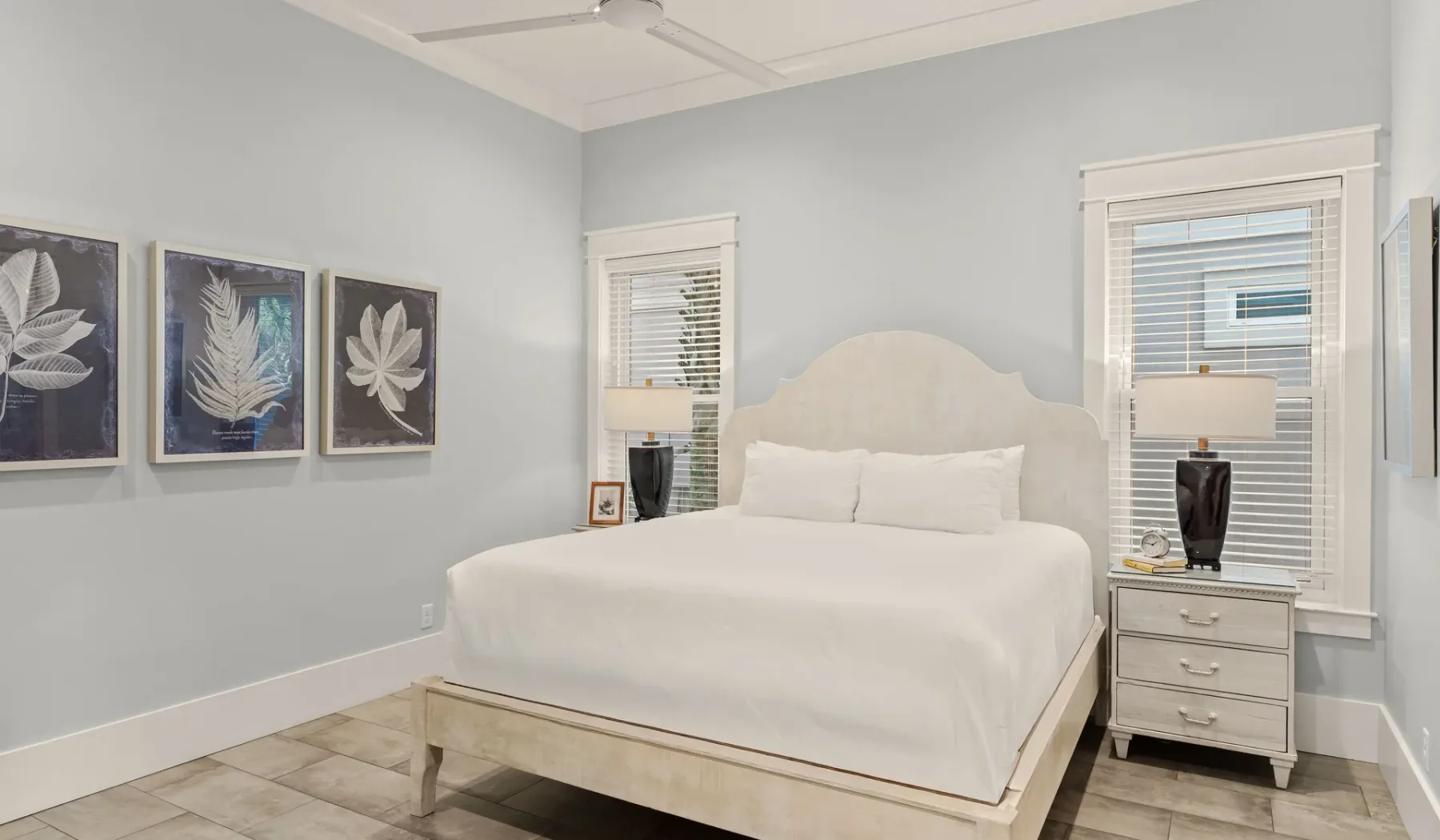 Dormitorio luminoso con una cama blanca, mesitas de noche y láminas botánicas enmarcadas.