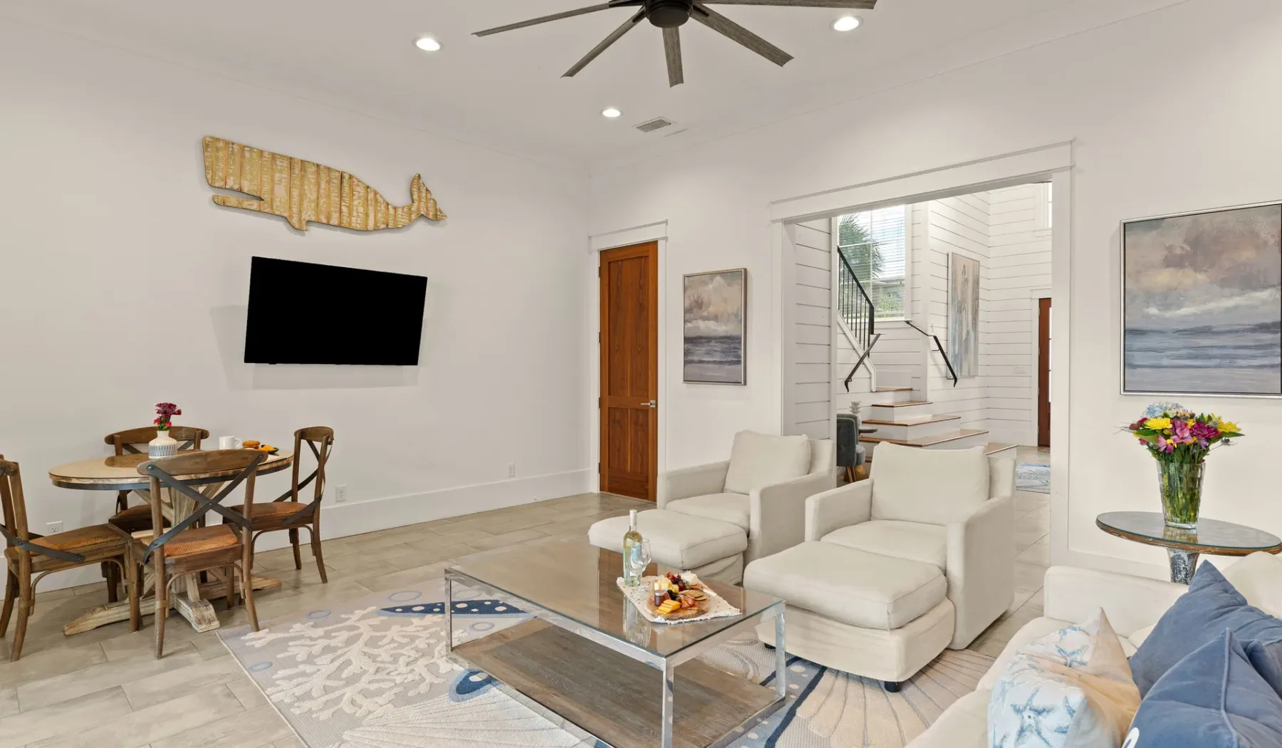 Una luminosa sala de estar y comedor con asientos, una mesa y un televisor en la pared.