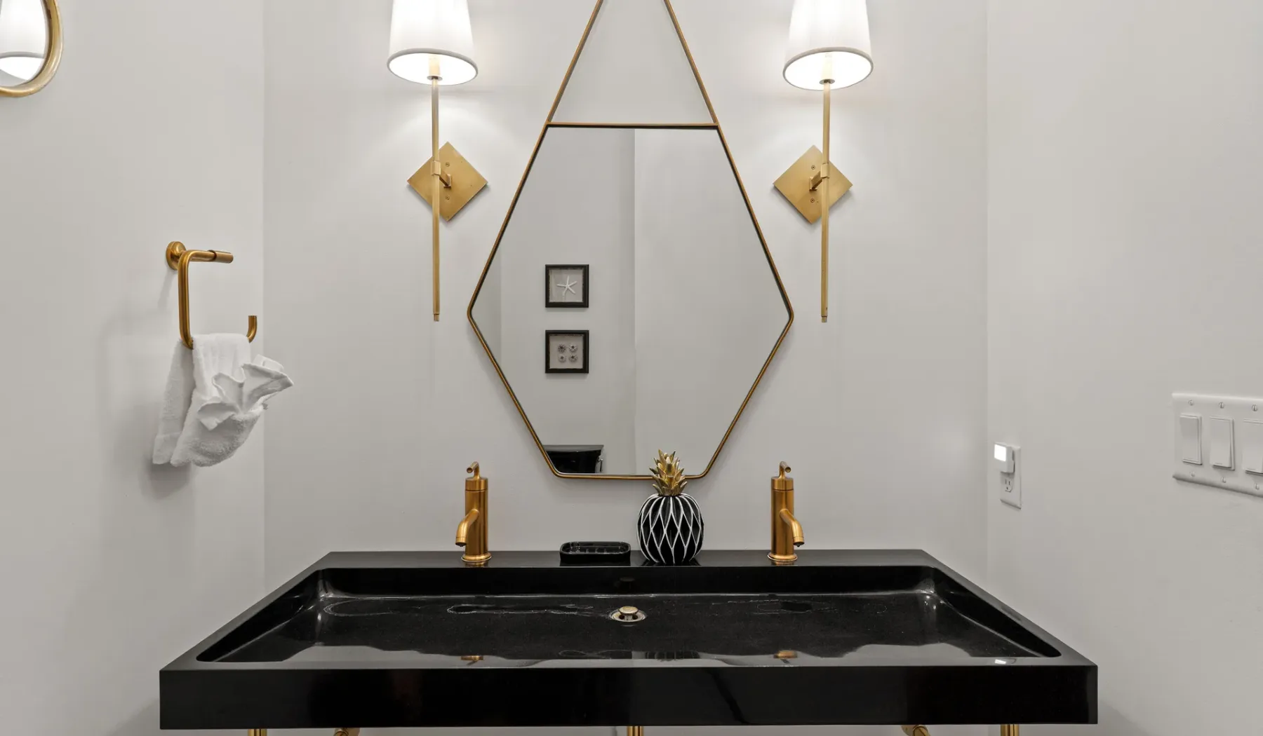 Un lavabo de baño con un amplio fregadero oscuro bajo un espejo geométrico.