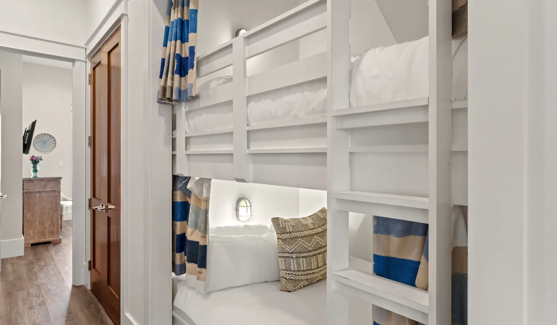 Una zona para dormir con literas, ropa de cama blanca y cortinas de rayas azules.