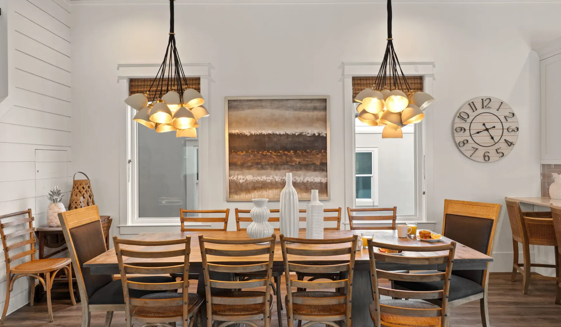 Un comedor con una mesa larga de madera, sillas y lámparas colgantes.