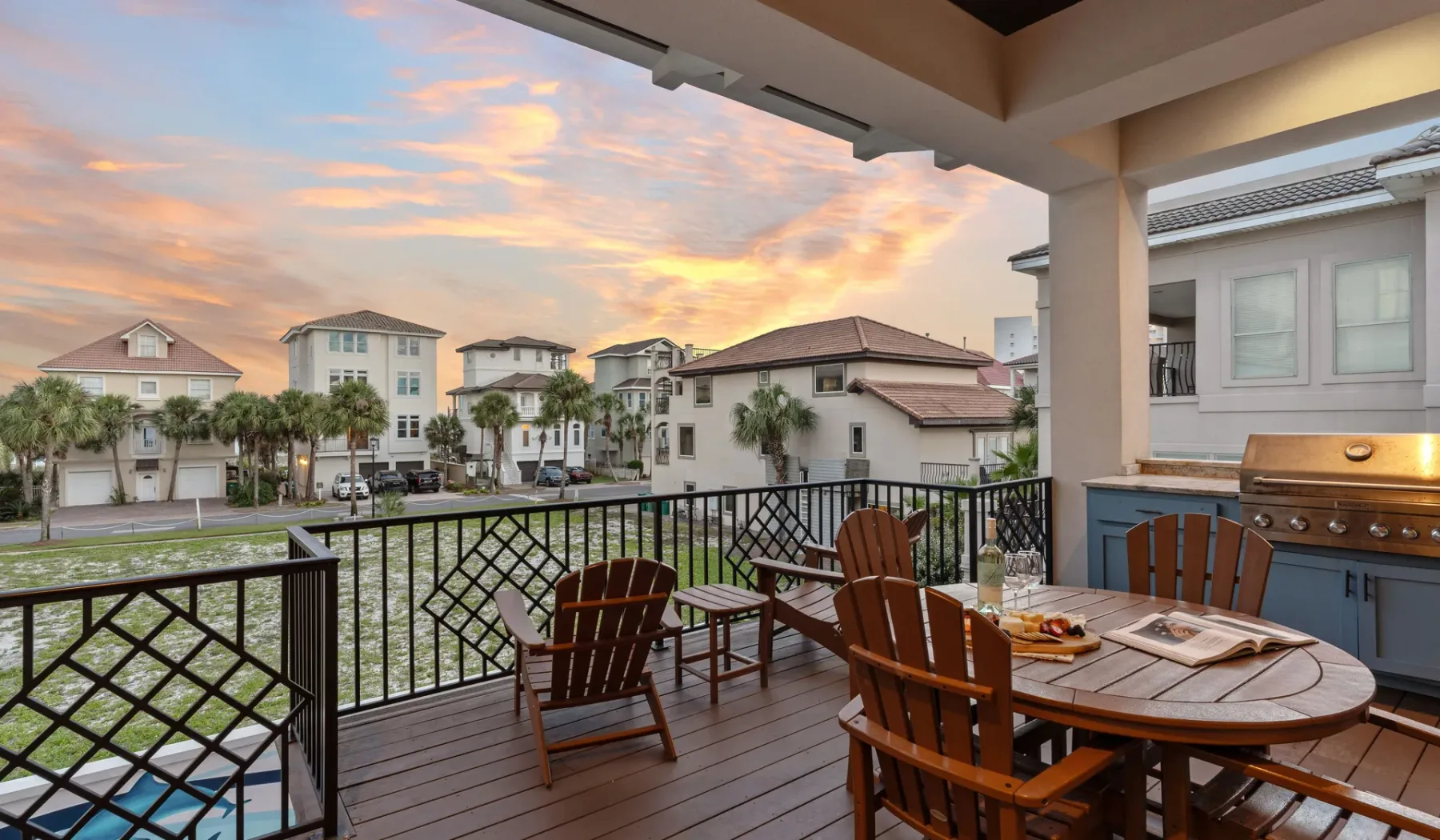 Un patio exterior cubierto da a casas vecinas al atardecer, con asientos y una mesa de comedor.