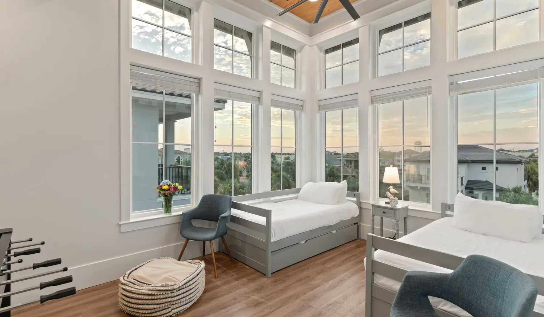 Un dormitorio luminoso con dos camas junto a ventanas altas con vistas al agua.
