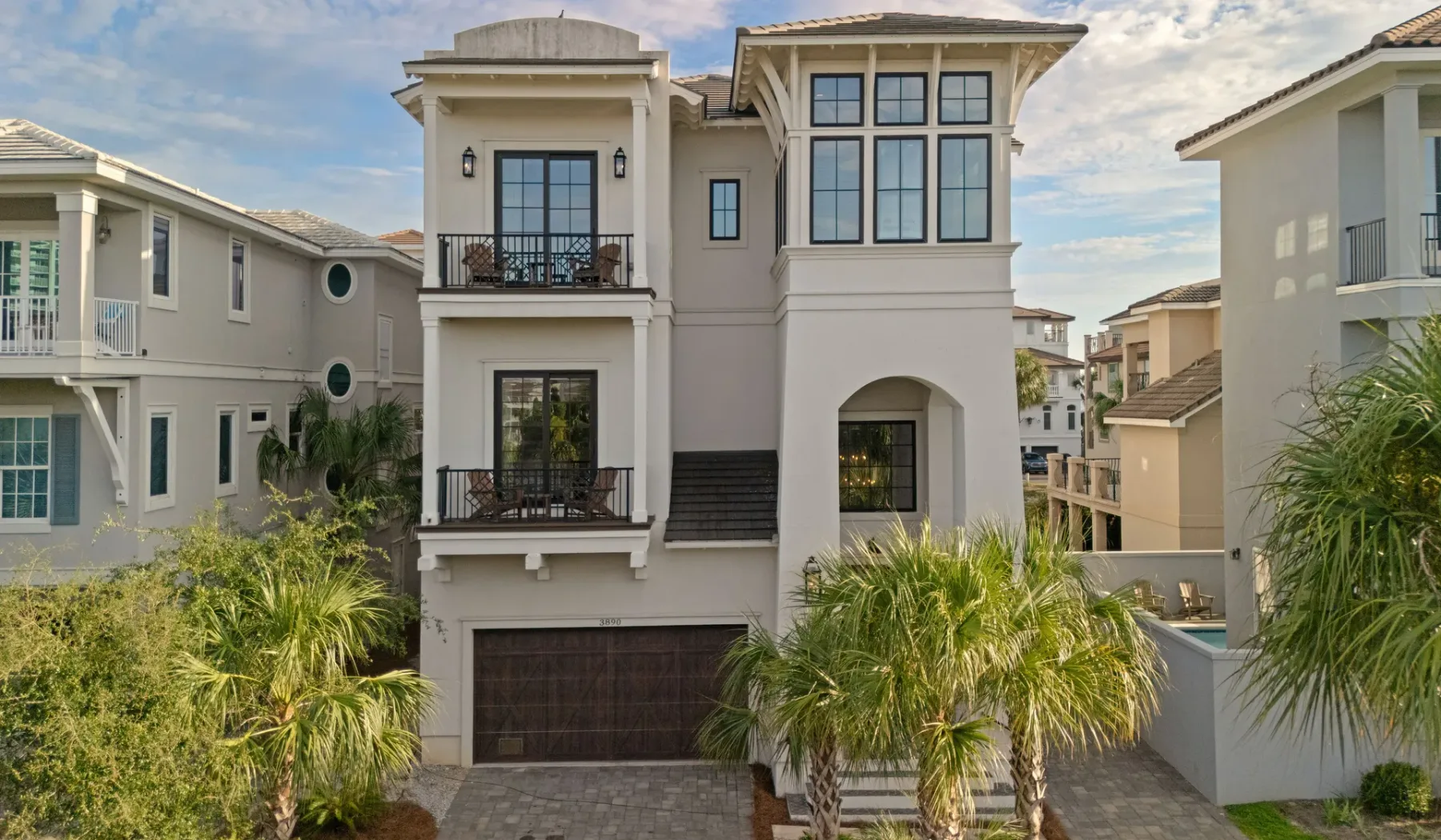Una casa grande de varios pisos se alza detrás de palmeras en una calle residencial.