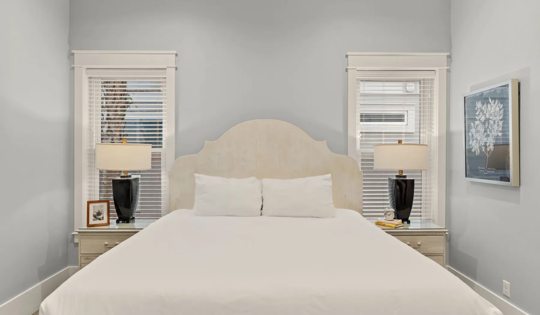 Un dormitorio luminoso con una cama entre dos ventanas.