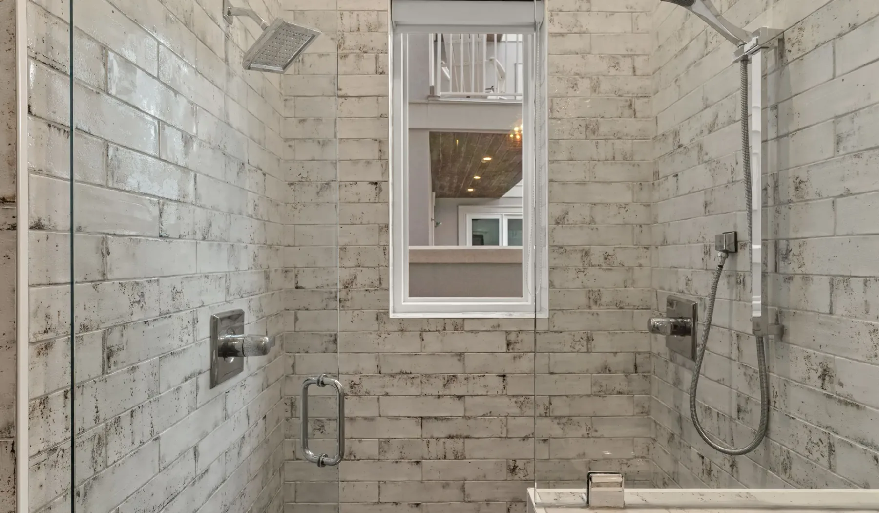 Zona de ducha de baño revestida de azulejos, con una ventana y accesorios en la pared.