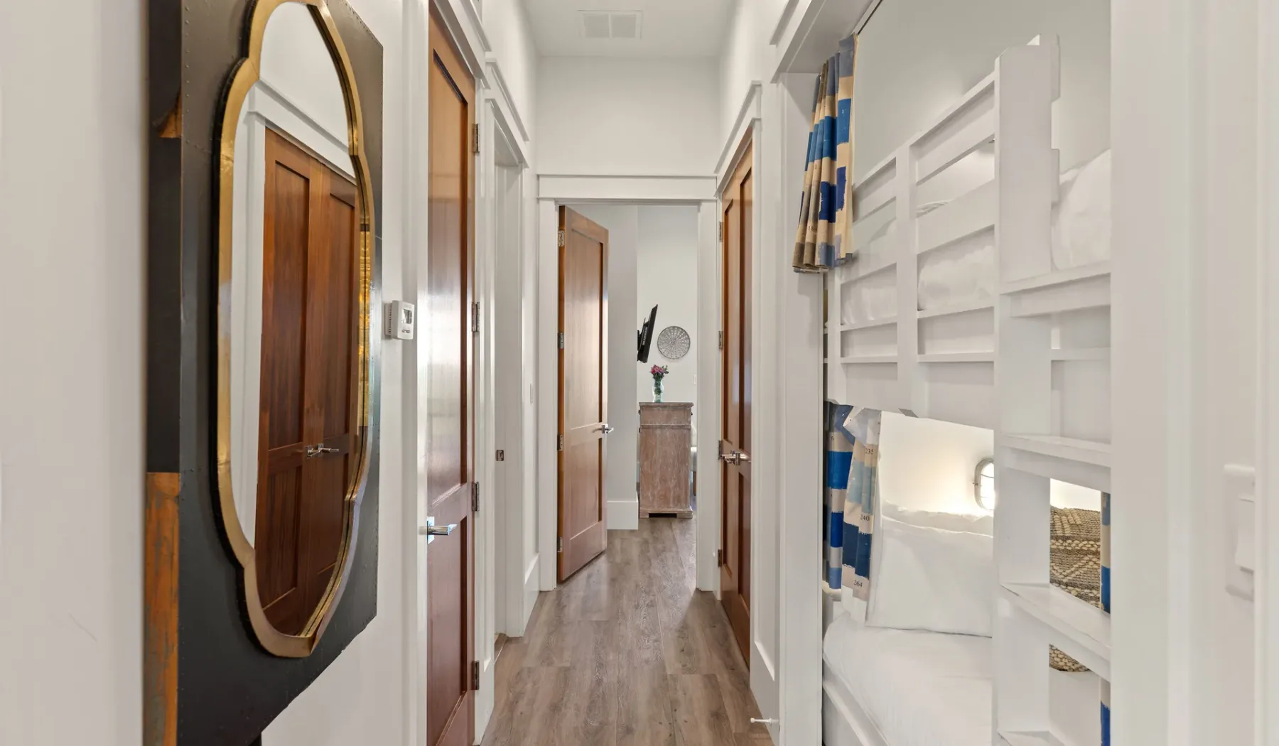Un pasillo luminoso con suelo de madera, varias puertas y una litera empotrada.