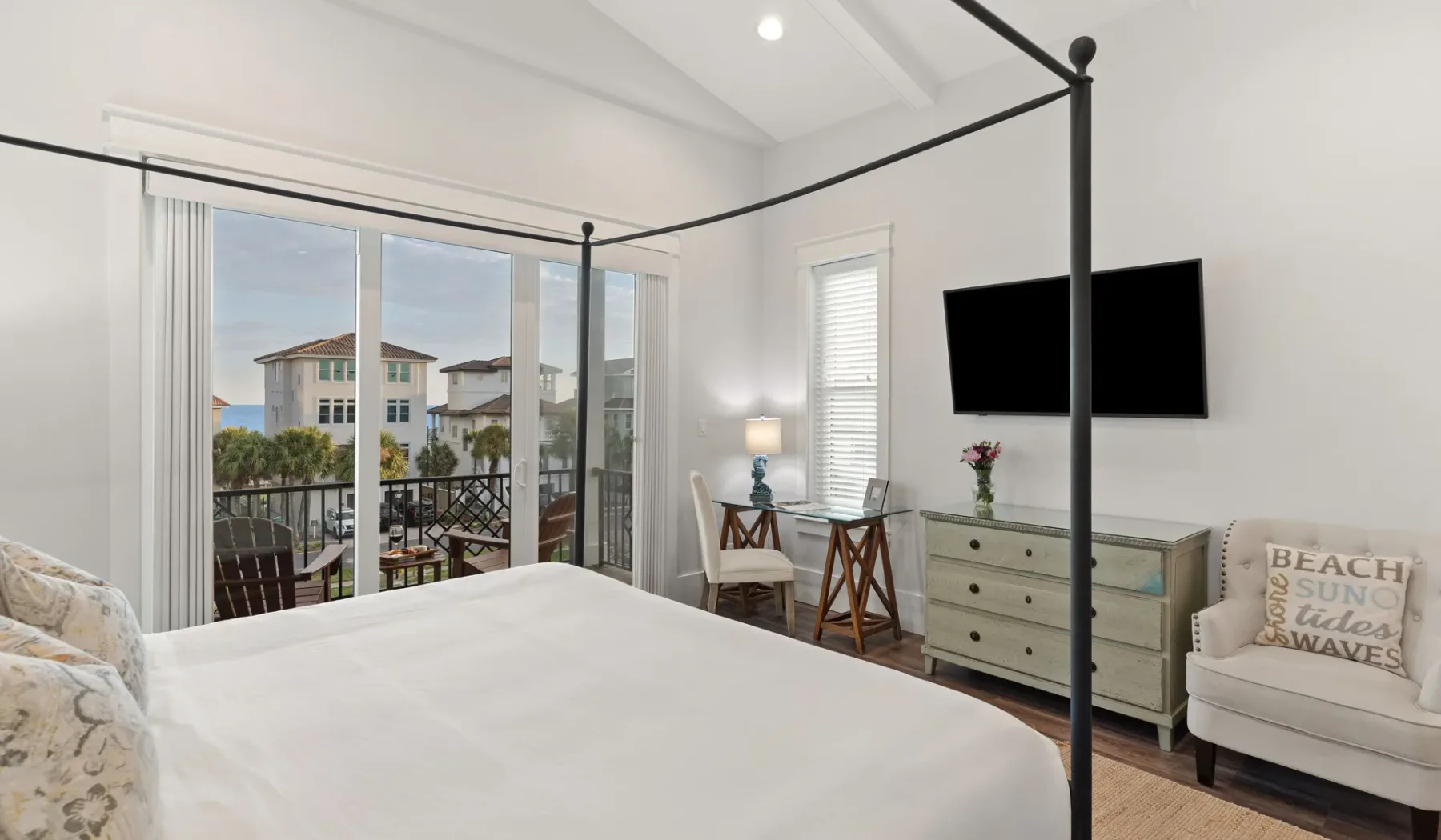 Un dormitorio luminoso con cama y asientos, y un balcón visible a través de puertas de vidrio.