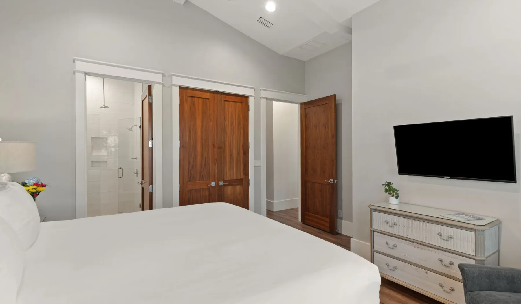 Un dormitorio con una cama, puertas de madera y un televisor en la pared.