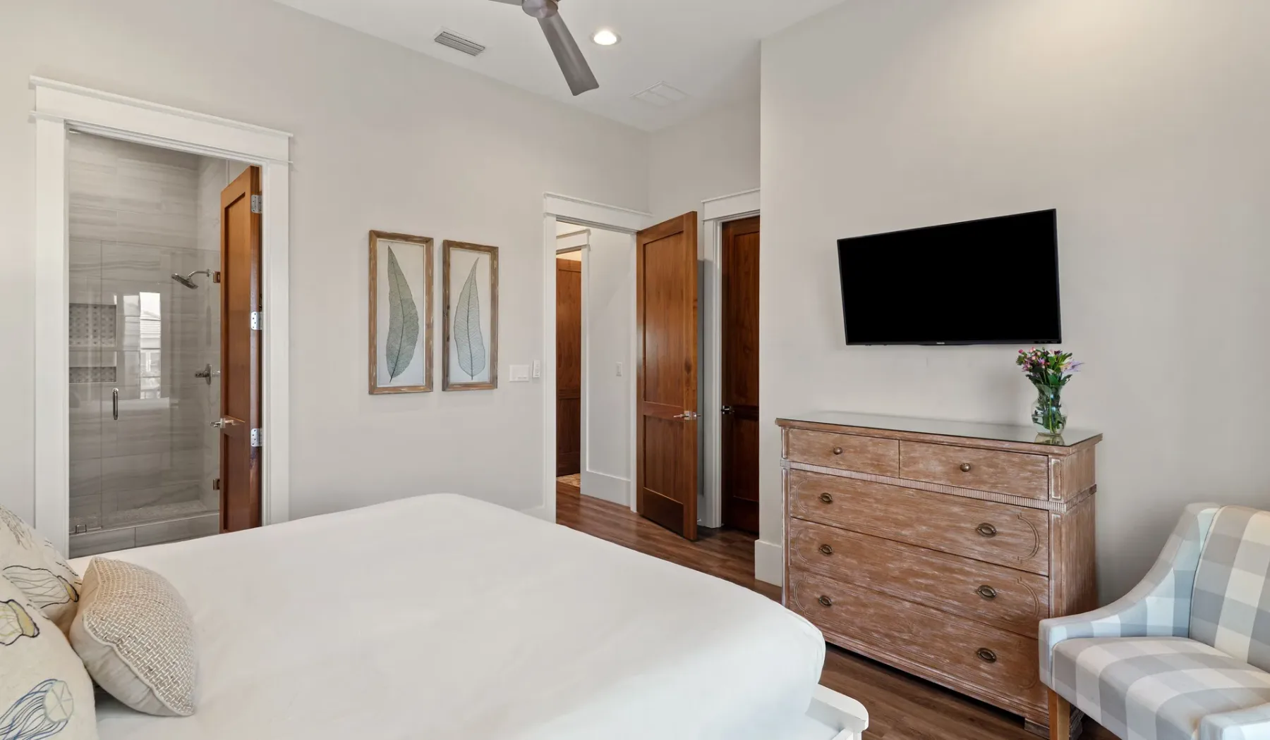 Un dormitorio con una cama, un televisor montado en la pared y una cómoda de madera.