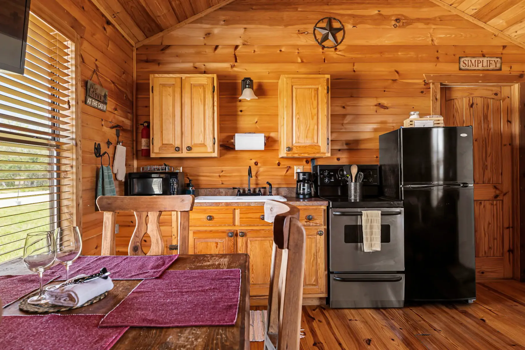 Acogedora cocina de cabaña de madera con cocina, refrigerador y zona de comedor. La iluminación cálida y la decoración rústica crean un ambiente acogedor.