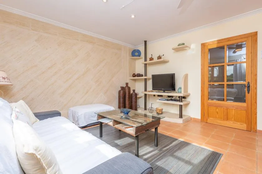 A living room with seating, a glass coffee table, and a television.