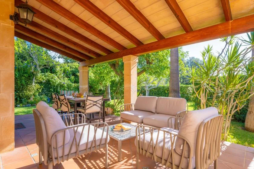 A covered outdoor patio with seating and a dining table overlooks a leafy garden.