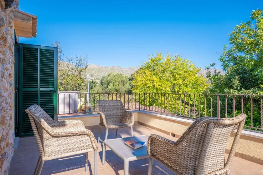 An outdoor terrace with woven seating overlooks leafy trees and distant hills.