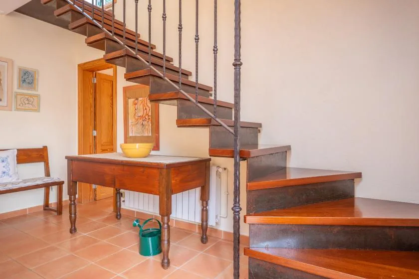 A tiled room with a wooden staircase and a table beneath it.