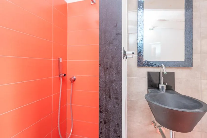 A bathroom with a bright orange tiled shower area and a vessel sink.
