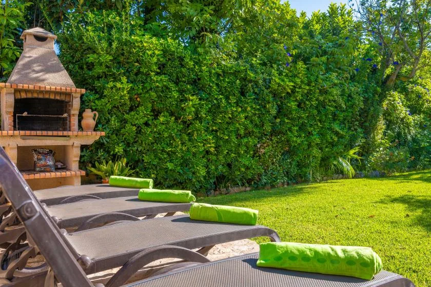 A garden patio has reclining loungers with bright green cushions beside a brick barbecue.