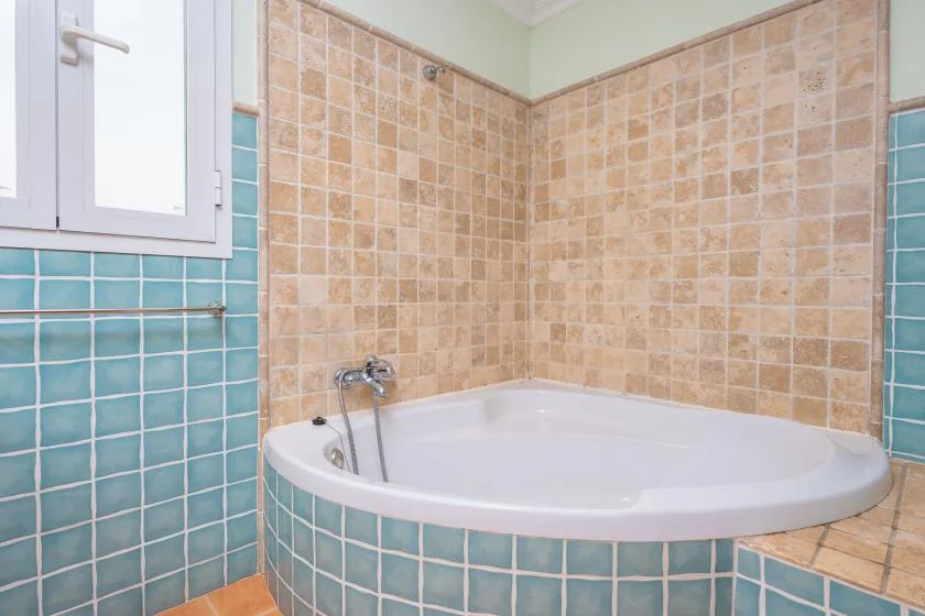 A tiled bathroom with a corner bathtub beneath a window.