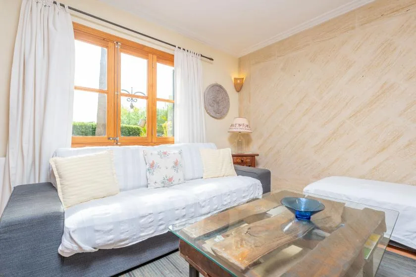 A bright living room with a white-covered sofa beneath a wooden-framed window.