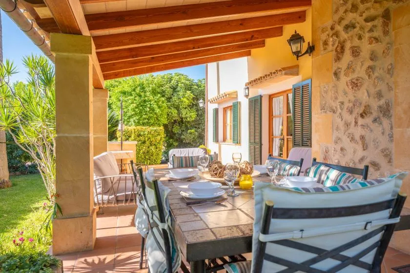 A covered outdoor dining patio with a table and cushioned seating beside the house.