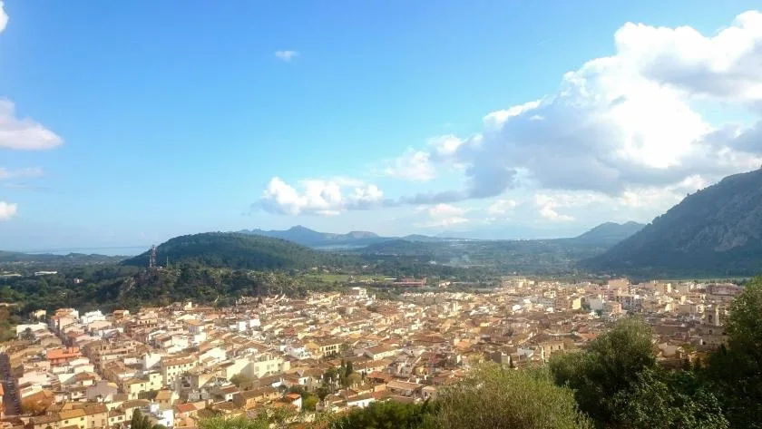 A town spreads across a valley beneath surrounding green hills and a bright sky.