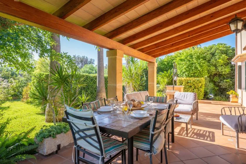 A covered outdoor dining area with a table, seating, and garden views.