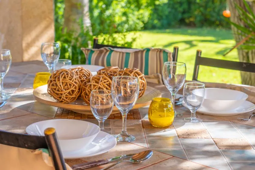 A patio dining table is set with plates, glasses, and a basket of bread.