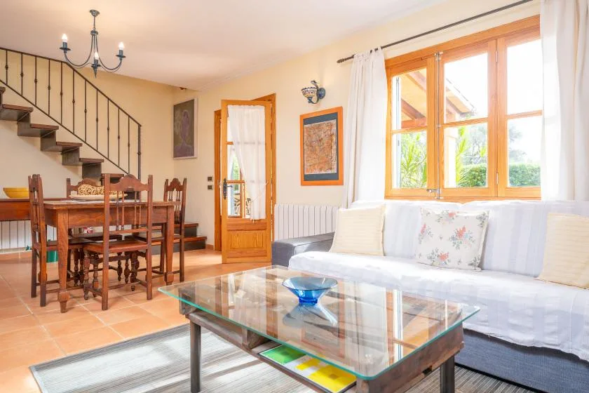 A bright living and dining area with a glass coffee table beside a wooden dining table.