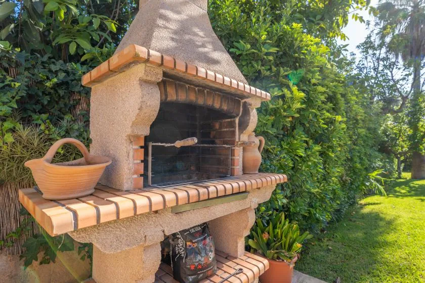 An outdoor brick barbecue grill stands among lush garden greenery.