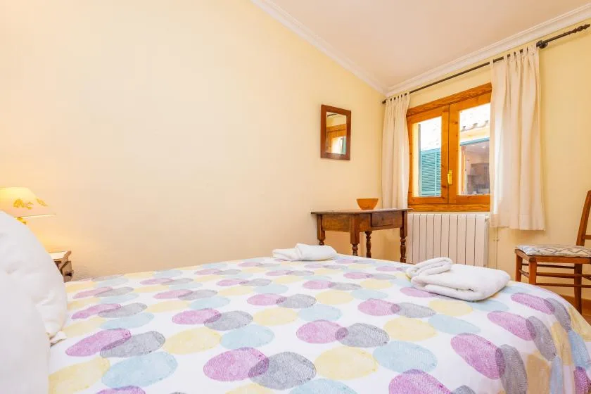 A bedroom with a colorful patterned bed beside a wooden-framed window.