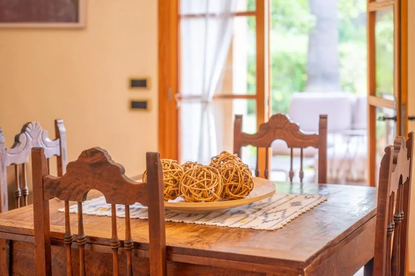 A wooden dining table with woven decorations sits beside open glass doors.