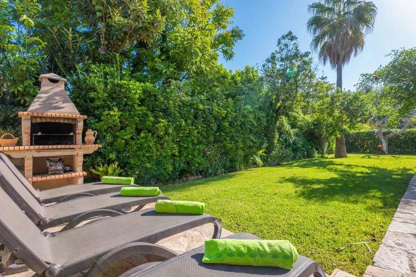 Un patio soleado con asientos de descanso, una barbacoa y césped verde.