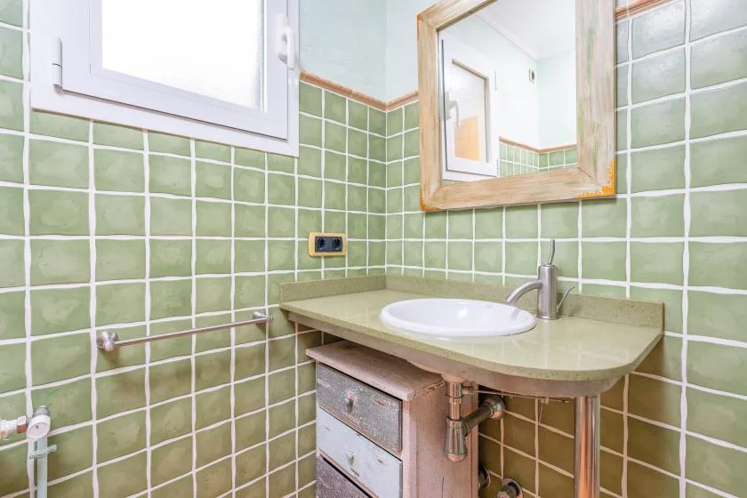 A bathroom vanity with a basin and mirror against green tiled walls.