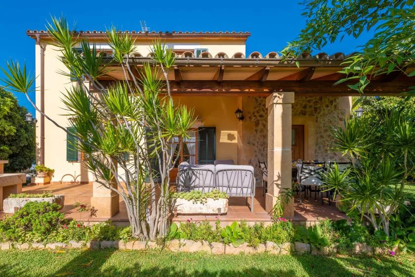 Exterior de una casa con patio sombreado, asientos al aire libre y plantas.