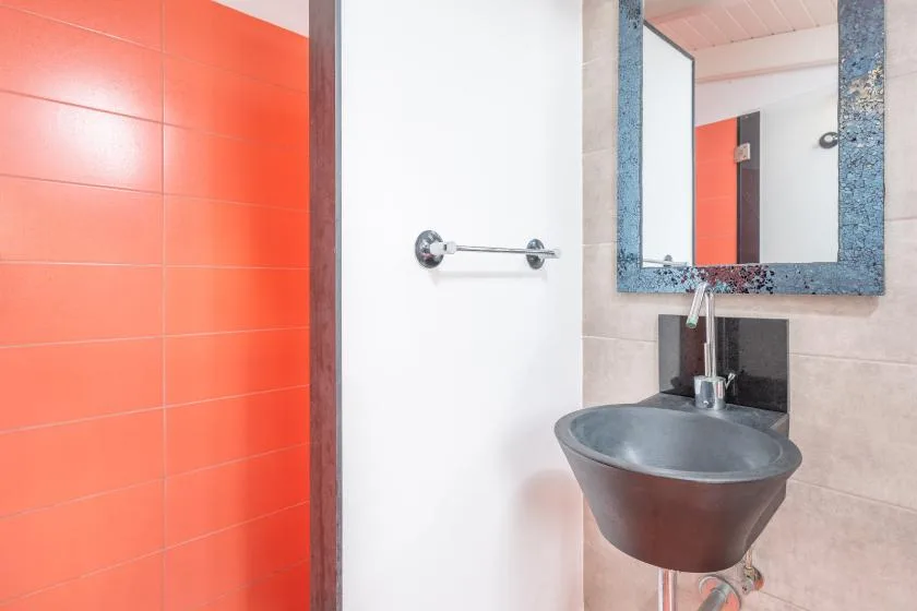 A bathroom with a wall-mounted sink and a bright orange tiled wall.