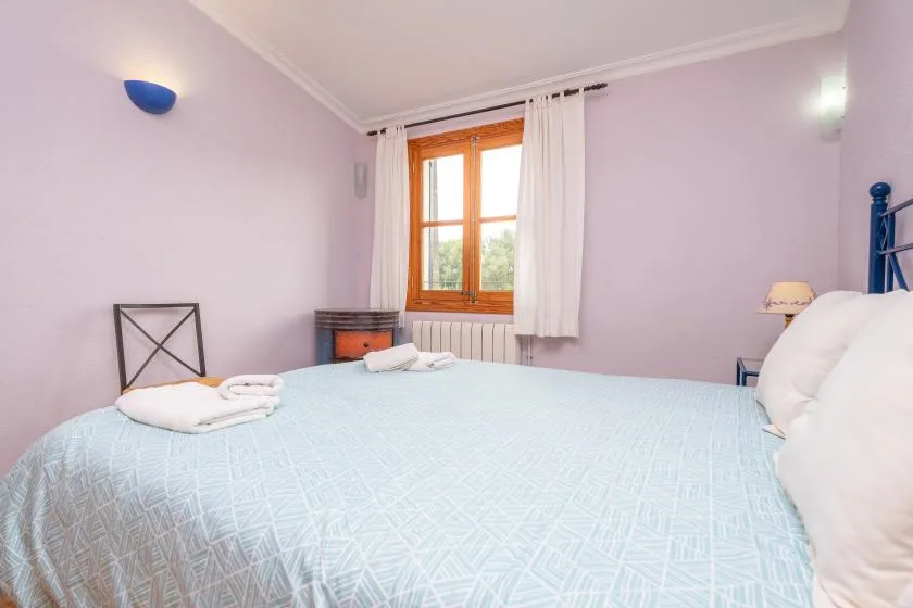 A bedroom with a bed beneath a window with white curtains.