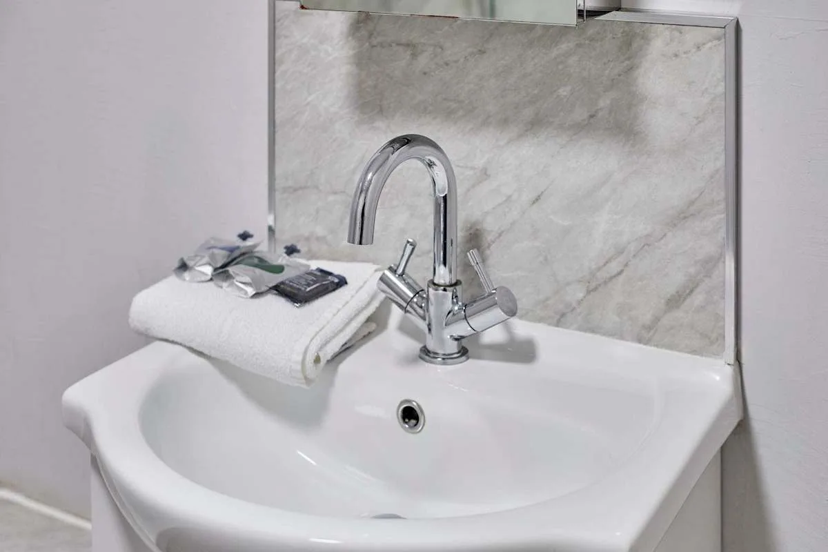 A bathroom sink with a curved faucet and folded white towels.