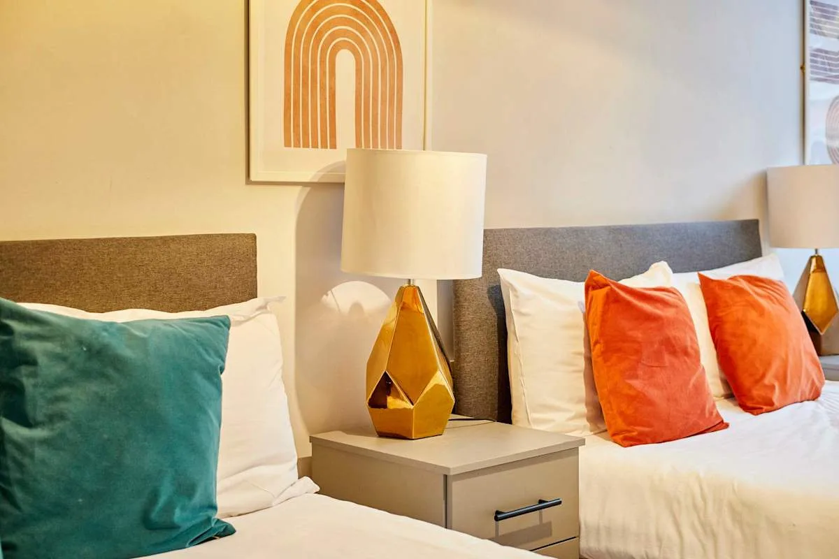 Bedroom with two beds, colorful pillows, and matching bedside lamps.